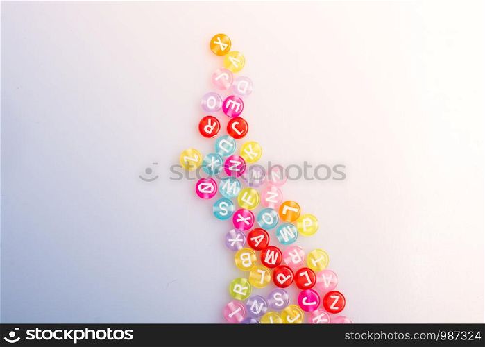 Multi color alphabet letter beads placed randomly on white background