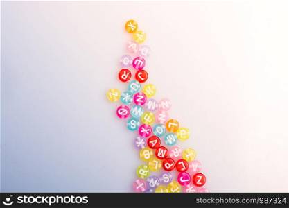 Multi color alphabet letter beads placed randomly on white background
