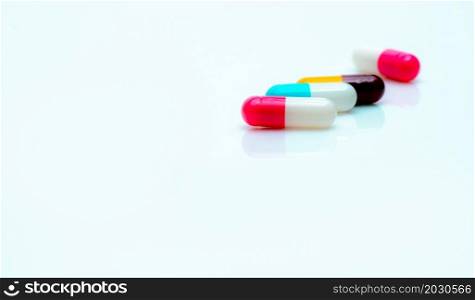 Multi-color antibiotic capsule pills on white background. Selective focus on pink and white capsule pill. Antibiotic drug resistance. Prescription drugs. Pharmaceutical industry. Antimicrobial drugs.