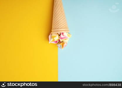 multi-colored baked meringues in a waffle cup on a blue-yellow background, flat lay