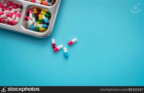 Multi-colored capsule pills in stainless steel tray and on blue background. Pharmacy banner. Pharmaceutical industry. Pharmaceutics. Prescription drugs. Medical and healthcare. Drug related problems.