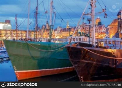 Multi-colored facades and boat on the central waterfront in Gdansk at night.. Gdansk. Central embankment at night.