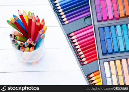 Multi colored pencils in jar on wooden table, with pastel and pencils box on background