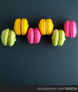 multi-colored round cakes with cream macarons on a black background, copy space