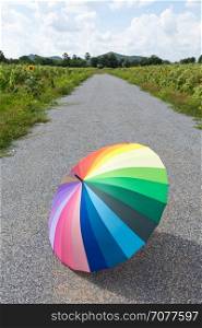 Multi-colored umbrella on the street. Sunflower field beside a road. Warmer weather and clear skies.