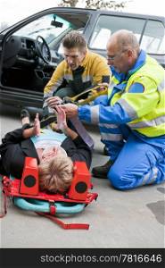 Multi-disciplinary medical team with a fireman and a paramedic, kneeling around a stretcher, and strapping an injured woman down