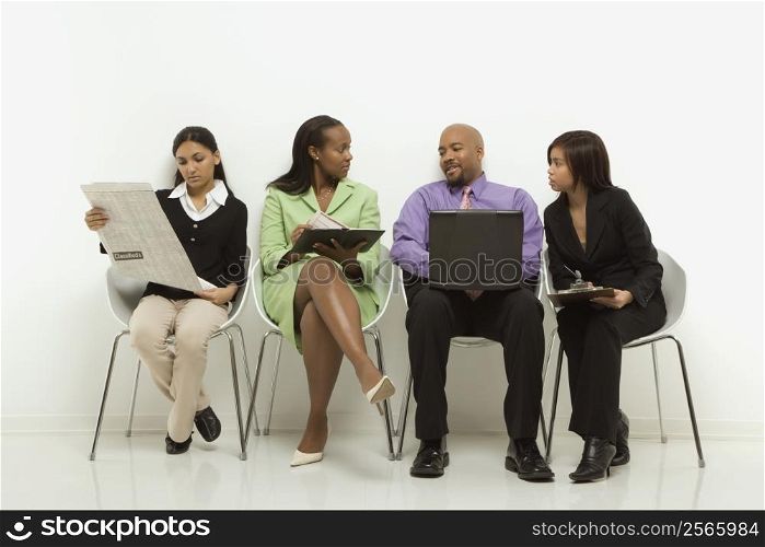 Multi-ethnic business group of men and women sitting looking at laptop and papers.