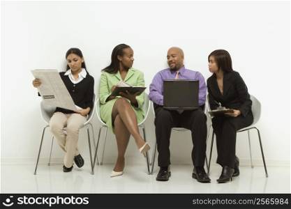 Multi-ethnic business group of men and women sitting looking at laptop and papers.
