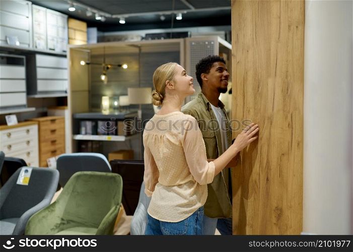 Multi-ethnic family couple buyer search wardrobe for new house apartment. Shopping in furniture shop. Multi-ethnic family couple searching wardrobe in shop