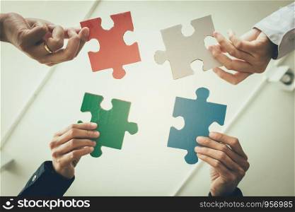 Multi-ethnic group of business professional putting four puzzle pieces together.