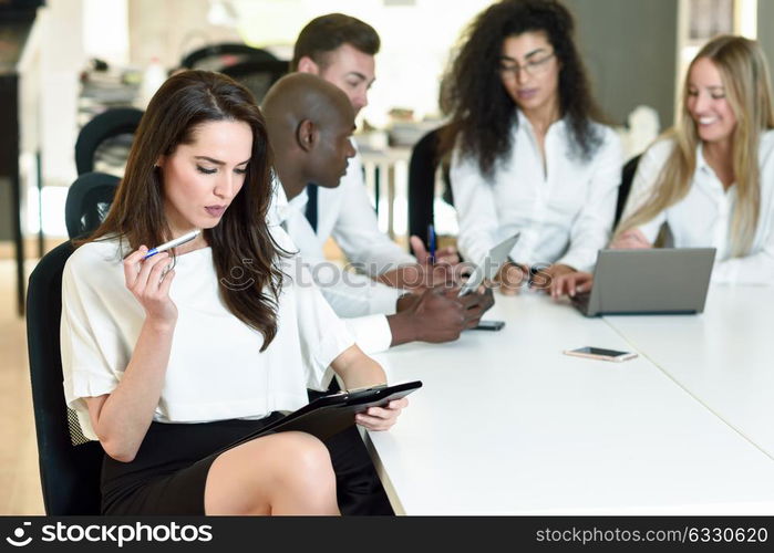 Multi-ethnic group of five businesspeople meeting in a modern office. Caucasian businesswoman leader, wearing white shirt and black skirt, looking at camera.