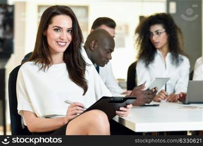 Multi-ethnic group of five businesspeople meeting in a modern office. Caucasian businesswoman leader, wearing white shirt and black skirt, looking at camera.