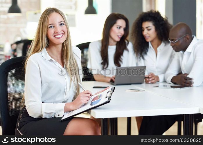 Multi-ethnic group of five businesspeople meeting in a modern office. Caucasian blonde businesswoman leader, wearing white shirt and black skirt, looking at camera.