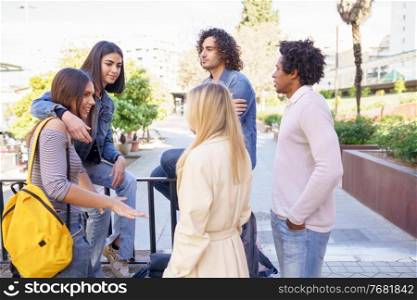 Multi-ethnic group of friends gathered in the street leaning on a railing. Young people having fun together.. Multi-ethnic group of friends gathered in the street leaning on a railing.