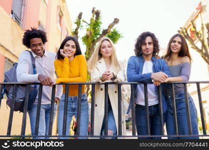 Multi-ethnic group of friends gathered in the street leaning on a railing. Young people having fun together.. Multi-ethnic group of friends gathered in the street leaning on a railing.