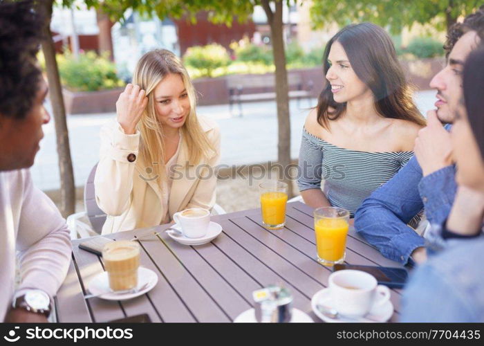 Multi-ethnic group of friends having a drink together in an outdoor bar. Young people having fun.. Multi-ethnic group of friends having a drink together in an outdoor bar.