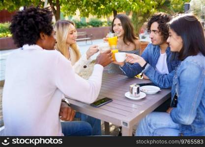 Multi-ethnic group of friends making a toast with their drinks while having a drink together at the outside table of a bar.. Multi-ethnic group of friends toasting with their drinks while having a drink together.