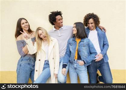 Multi-ethnic group of friends posing while having fun and laughing together against a yellow urban wall.. Multi-ethnic group of friends posing while having fun and laughing together