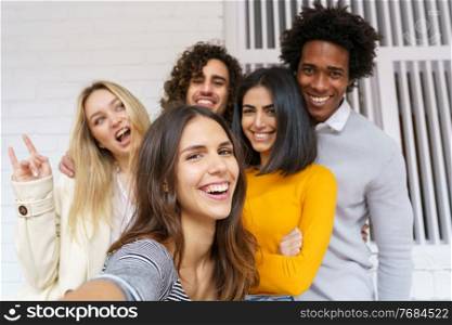 Multi-ethnic group of friends taking a selfie together while having fun in the street. Caucasian girl in the foreground.. Multi-ethnic group of friends taking a selfie together while having fun outdoors.