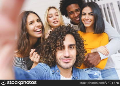 Multi-ethnic group of friends taking a selfie together while having fun in the street. Arab man with afro hair in the foreground.. Multi-ethnic group of friends taking a selfie together while having fun outdoors.