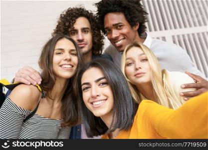 Multi-ethnic group of friends taking a selfie together while having fun in the street. Persian woman in the foreground.. Multi-ethnic group of friends taking a selfie together while having fun outdoors.