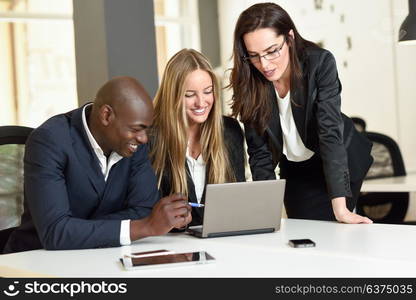 Multi-ethnic group of three businesspeople meeting in a modern office. Two caucasian women and a black man wearing suit looking at a laptop computer.