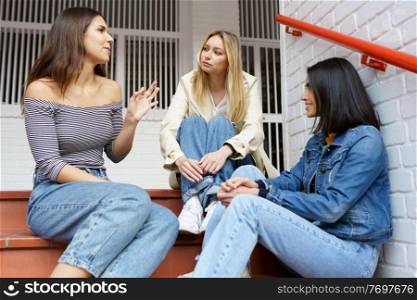 Multi-ethnic group of three female friends sitting on street steps talking.. Multi-ethnic group of three friends sitting on street steps talking.
