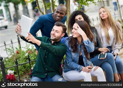 Multi-ethnic group of young people taking selfie photograph together outdoors. Beautiful funny women and men wearing casual clothes in urban background.