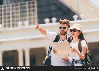 Multi-ethnic traveler couple using local map together on sunny day, man pointing forward to copy space. Honeymoon trip, backpacker tourist, Asia city tourism, or summer holiday vacation travel concept