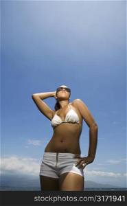Multi ethnic young adult woman standing on beach in bikini.