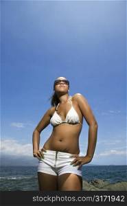 Multi ethnic young adult woman standing on beach in bikini.