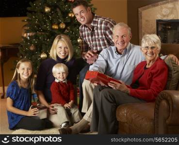 Multi Generation Family Opening Christmas Presents In Front Of Tree