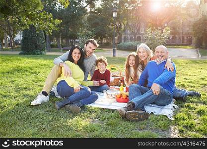 Multi generation family sitting on grass having picnic, looking at camera smiling