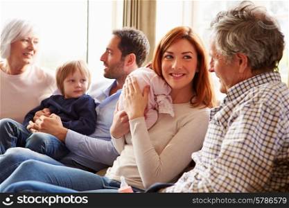 Multi Generation Family Sitting On Sofa With Newborn Baby