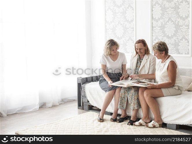 multi generation women looking album together while sitting sofa