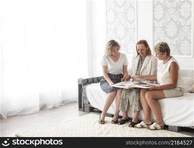 multi generation women looking album together while sitting sofa