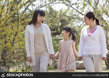 Multi-generational family, grandmother, mother, and daughter holding hands and going for a walk in the park in springtime