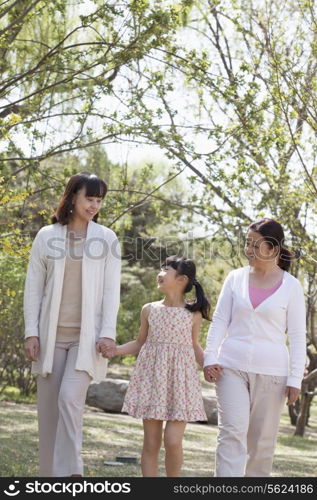 Multi-generational family, grandmother, mother, and daughter holding hands and going for a walk in the park in springtime