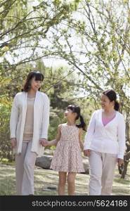 Multi-generational family, grandmother, mother, and daughter holding hands and going for a walk in the park in springtime