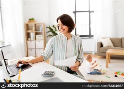 multi-tasking, freelance and motherhood concept - mother working with papers at laptop computer and baby boy at home office. mother working at laptop and baby playing at home