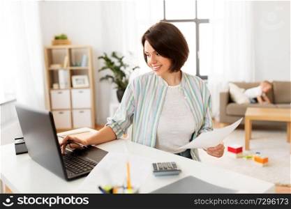 multi-tasking, freelance and motherhood concept - mother working with papers at laptop computer and baby boy at home office. mother working at laptop and baby boy at home
