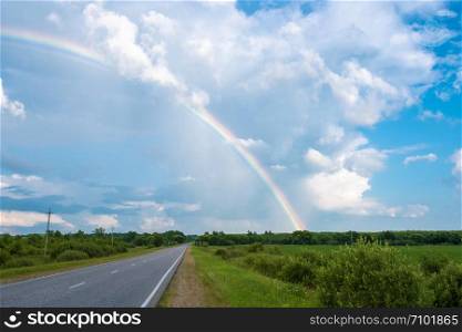 Multicolor rainbow against the cloudy sky and wet asphalt road, Russia.
