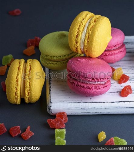 multicolored baked cakes of almond flour macarons on a white wooden board, black background, close up. multicolored baked cakes of almond flour macarons