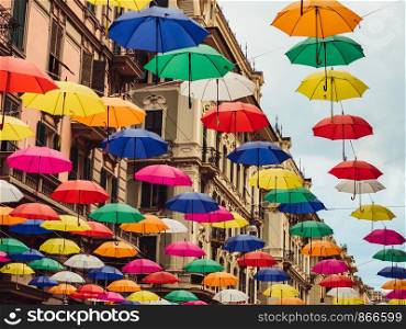 Multicolored, bright umbrellas hanging between houses on the beautiful, narrow streets of the magnificent city of Genoa against the blue sky, on a sunny, summer day. Concept of travel and recreation. Multicolored and bright umbrellas hanging between houses
