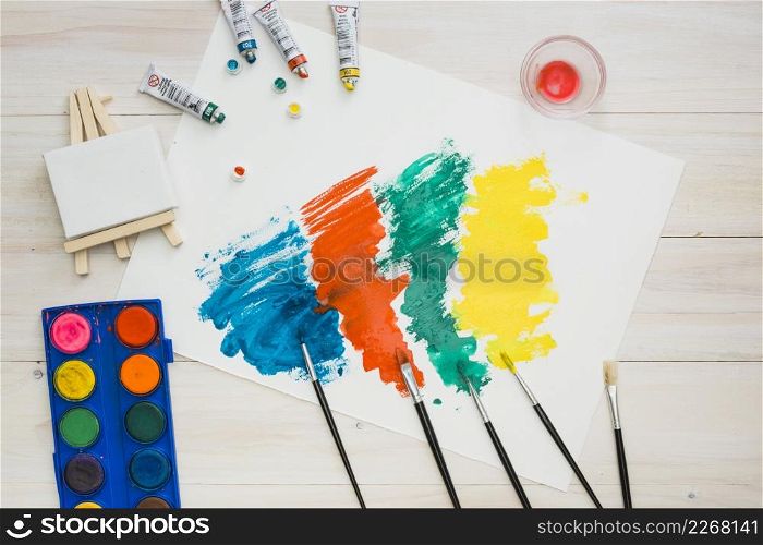 multicolored brushstroke white page with painting equipment wooden table