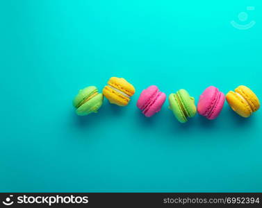 Multicolored cake of almond flour with cream macarons lie in a row on a blue background, macarons in the middle, top view, an empty space on the left, vintage toning