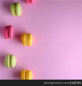 multicolored cakes of almond flour with cream lie in a row on a pink background, copy space