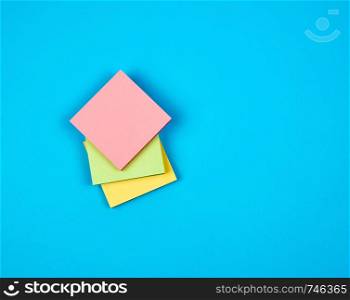 multicolored empty paper square stickers on blue background, copy space