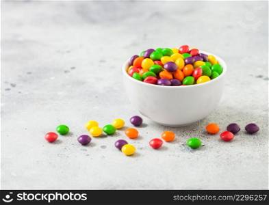Multicolored fruit candies in white bowl on light background