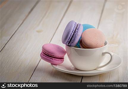 Multicolored macaroons in white cup on wooden table. Macaroons in cup on wooden table